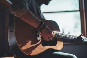 Person playing acoustic guitar indoors near window.