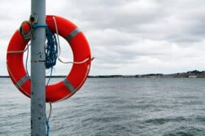 Life buoy on a pole by the water's edge, overcast sky, coastal landscape in the background.